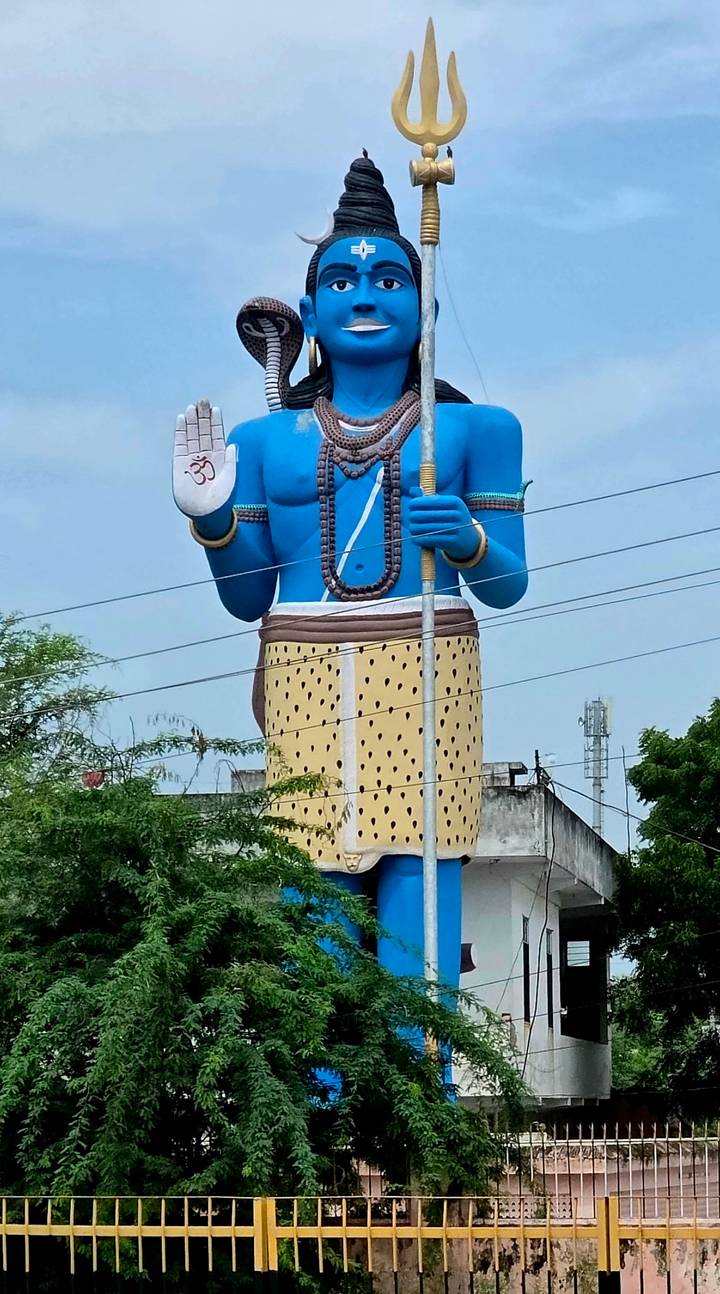 Huge blue Hanuman statue holding a mace towering above treetops and rooftops