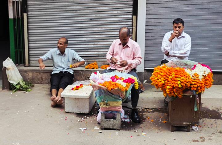 Flower vendors sitting beside piles of bright orange marigold garlands on a city street