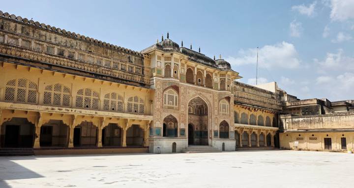 Sunny courtyard of Amber Fort featuring ornate archways and patterned windows