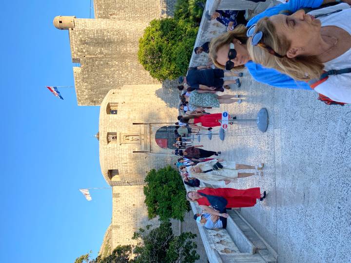 Crowds of tourists crossing the stone bridge into Dubrovnik’s fortified city gate on a sunny day.
