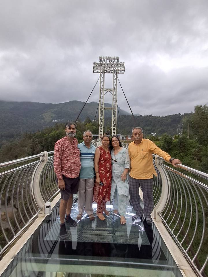 Family group posing on a metal suspension glass bridge with misty hills behind.