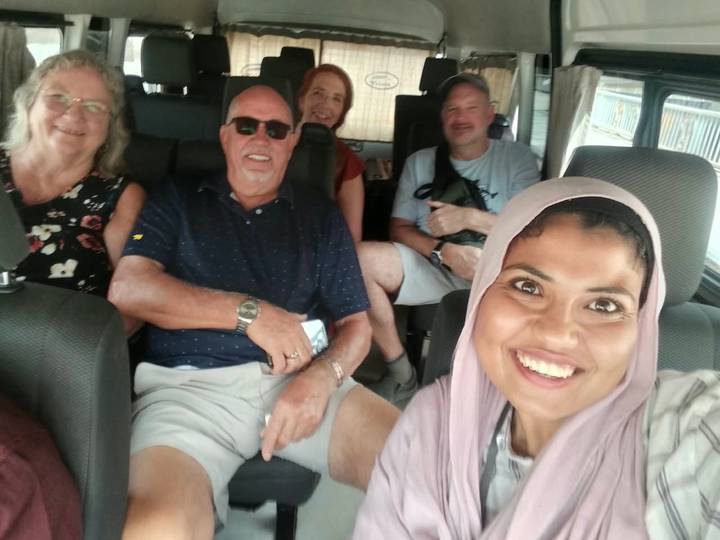 Smiling guide snapping a selfie with four seated tourists inside a minivan.
