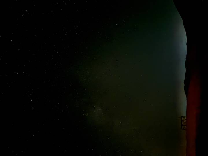 Star-filled night sky over a dark desert horizon with faint silhouettes of dunes.