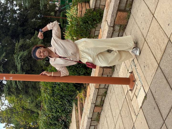Young woman posing playfully beside a lamp post in a leafy urban park.