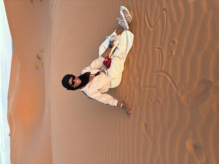 Traveller sitting relaxed on the warm sand of a vast dune holding a water bottle.