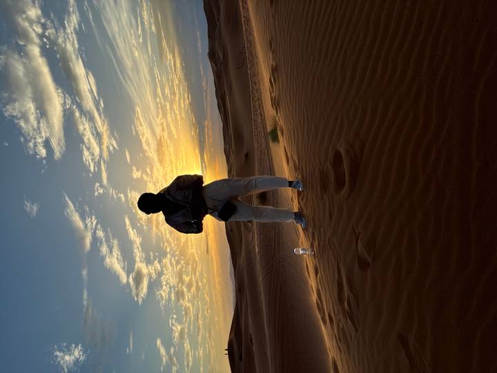 Silhouette of a woman standing on a cresting dune watching the colourful desert sunset.