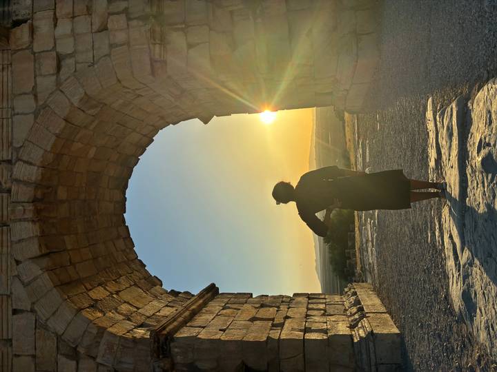 Back-lit view of a woman framed by a stone arch at sunset in Volubilis.