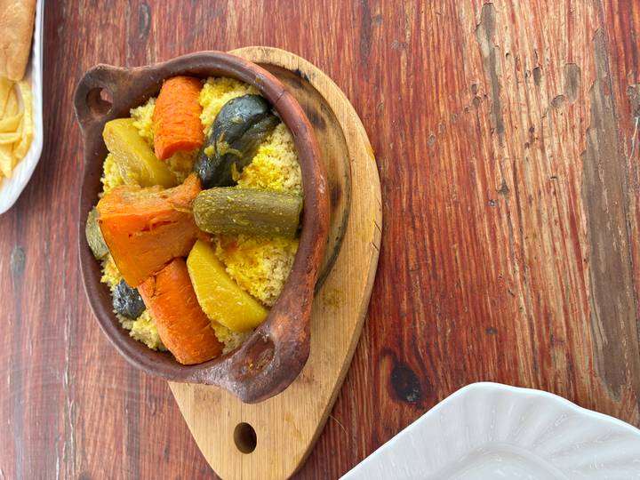 Traditional vegetable couscous tagine in a clay pot on a rustic wooden table.