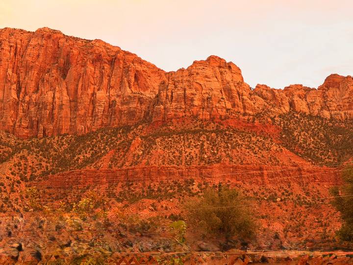 Towering rust-coloured sandstone cliffs rise dramatically against a pale sky in the desert Southwest.