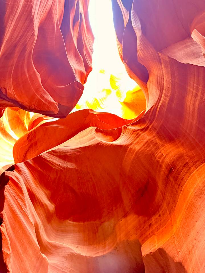 Vibrant curves of Antelope Canyon twist upward toward a burst of glowing light.