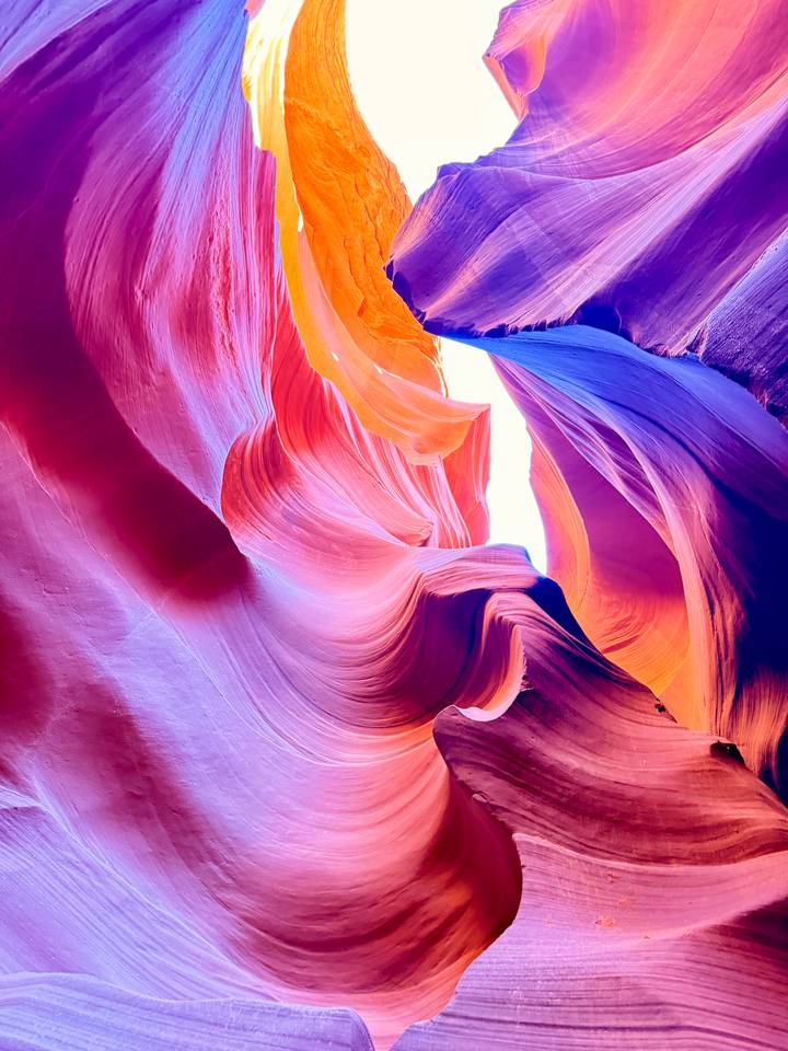 Multicoloured sandstone waves ripple gracefully toward a bright opening overhead.