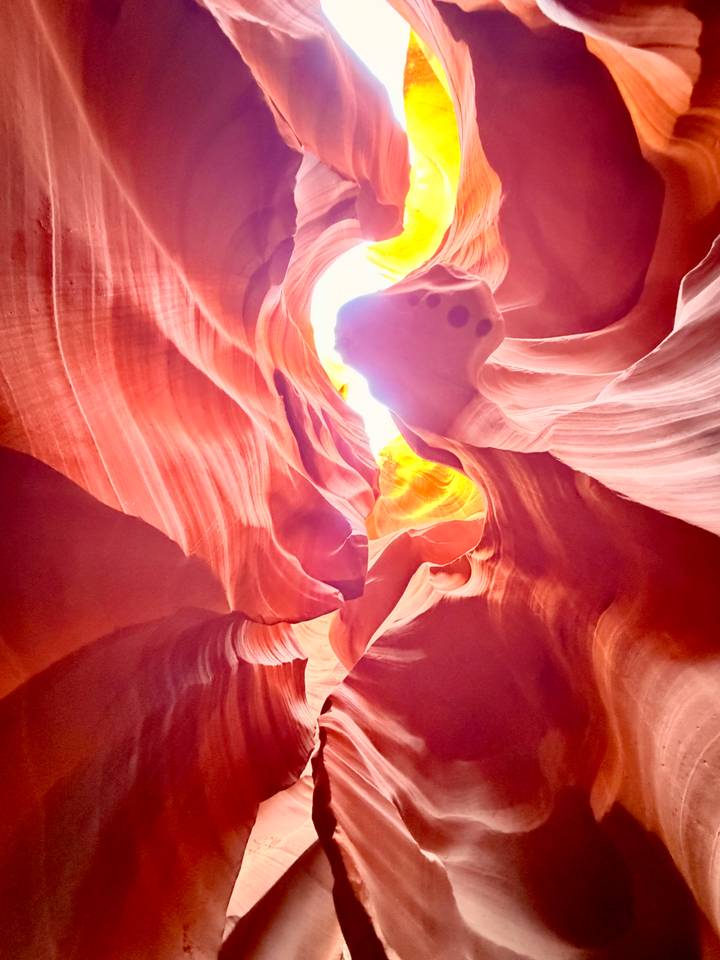 Soft light illuminates swirling pink and gold sandstone chambers inside a slot canyon.