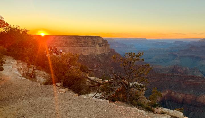 The sun sets over the vast layered chasms of the Grand Canyon, casting golden light across the rim.