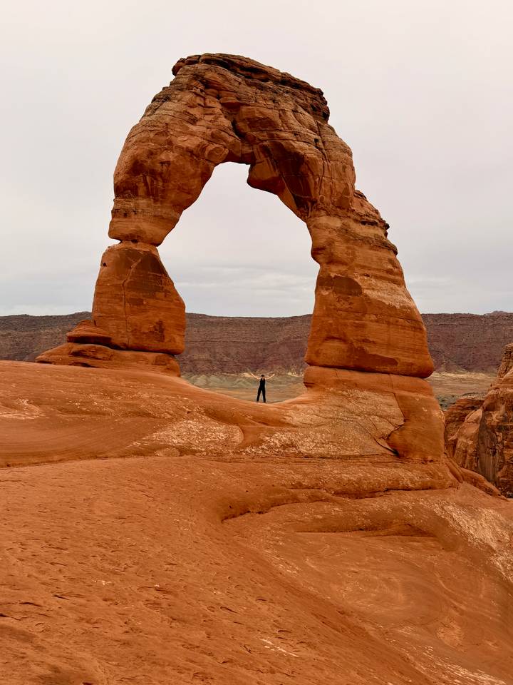 A lone traveller stands beneath Delicate Arch, dwarfed by the iconic sandstone span.