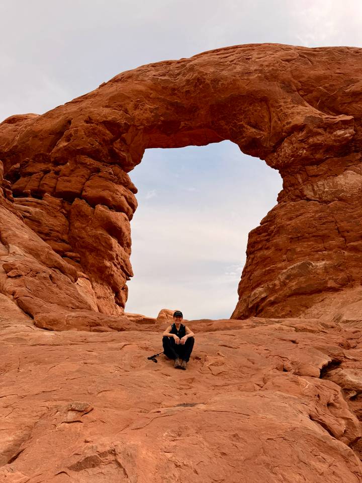 A traveller sits between massive sandstone walls of a natural arch, gazing upward.