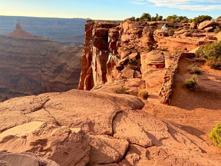Sunlit sandstone ledges overlook a vast canyon landscape dropping away into the distance.