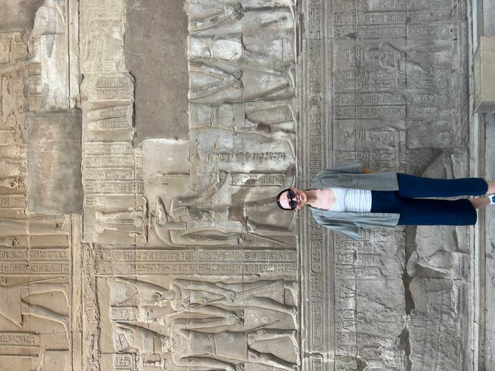 Smiling traveller poses before intricate hieroglyphic wall inside ancient temple