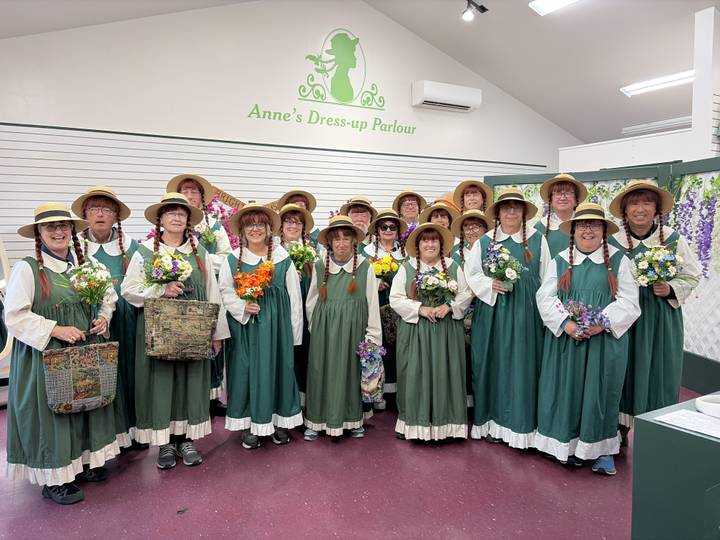 Large group dressed in matching green prairie dresses and straw hats holding bouquets.