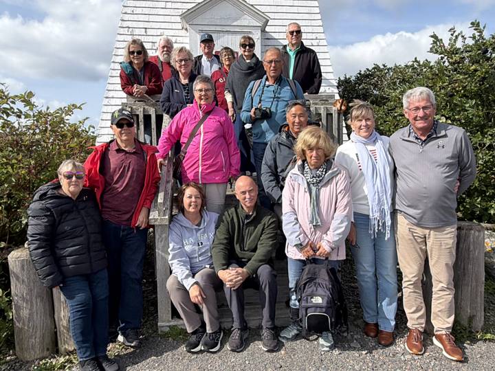 Tour group posing on wooden steps beside a small white lighthouse structure.