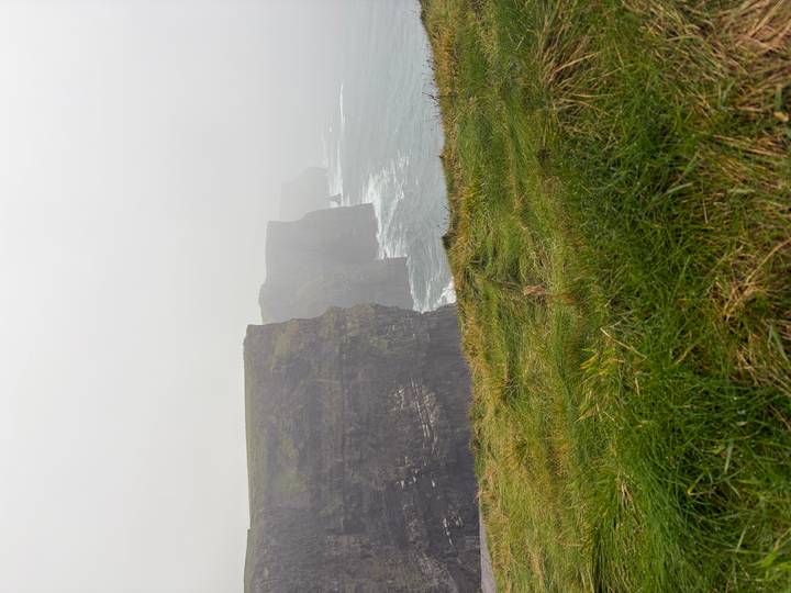 Iconic sea cliffs disappearing into misty fog with waves crashing below