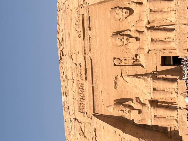 Massive seated statues of Ramses II dominate the rock-cut façade of Abu Simbel under clear sky.