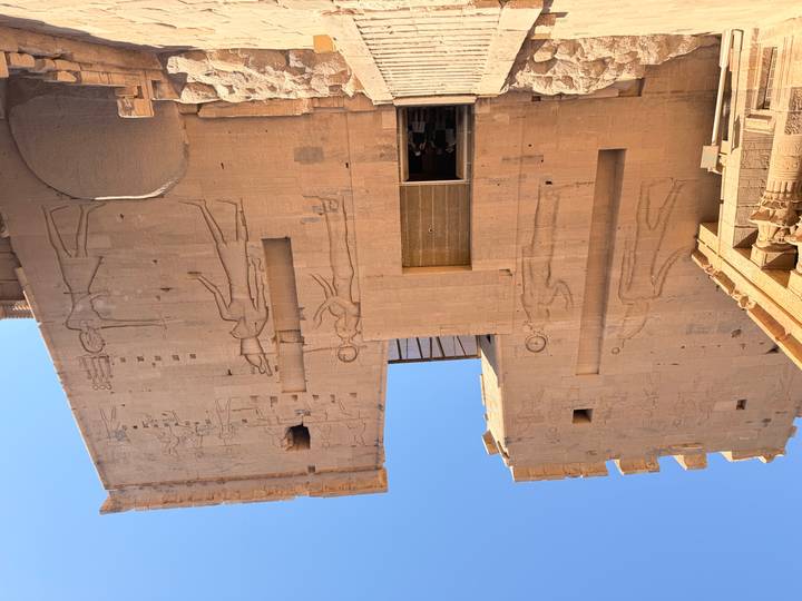 Sandstone walls of Philae Temple rise against blue sky; visitors stand in the doorway.