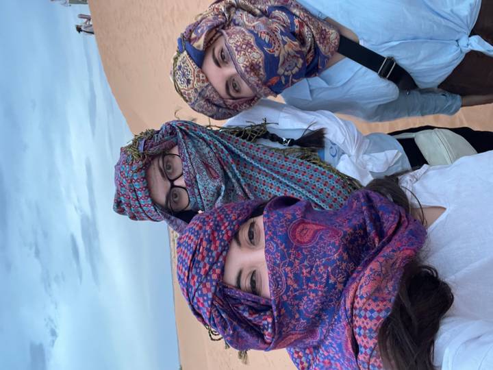 Three travellers with patterned scarves covering faces take a desert selfie against sand dunes.