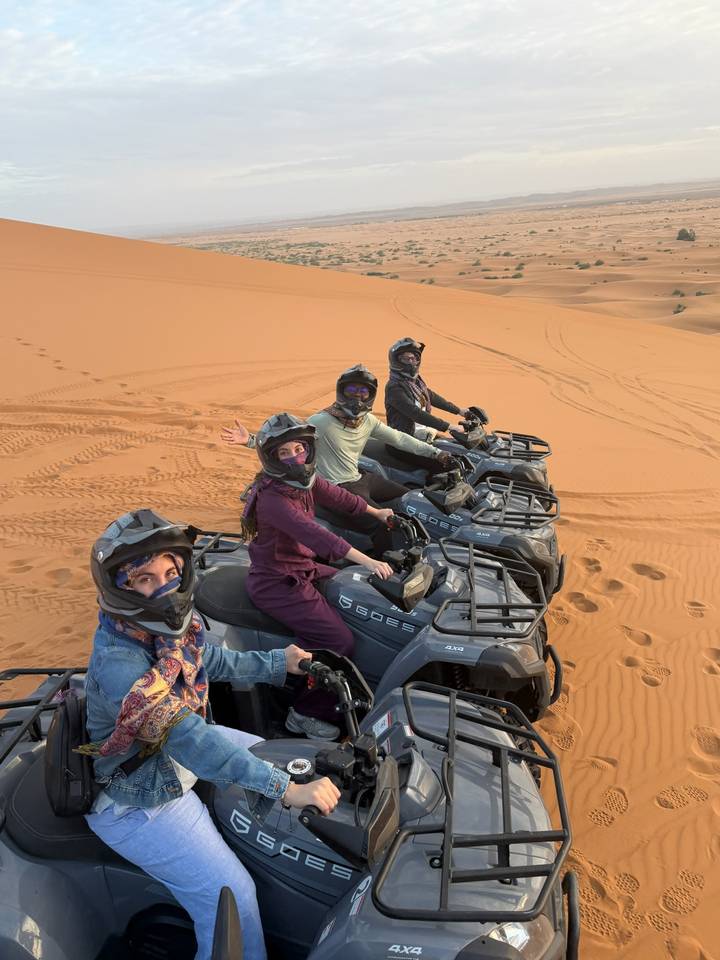 Riders grin from their quad bikes lined up on patterned desert sand.