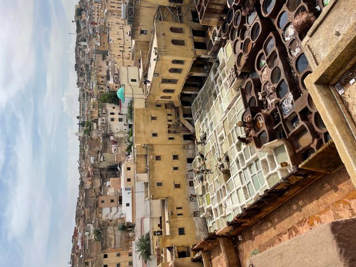 Overlook of Fes tannery pits with workers treating leather amid earthy yellow buildings.