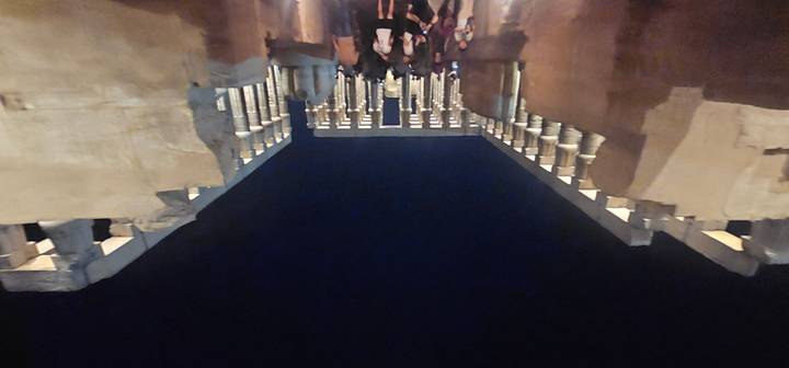 Blurry night photo of illuminated colonnade at Luxor Temple with tourists walking through.