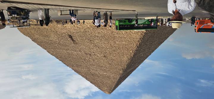 Great Pyramid of Giza towers over visitors and tour buses under partly cloudy sky.
