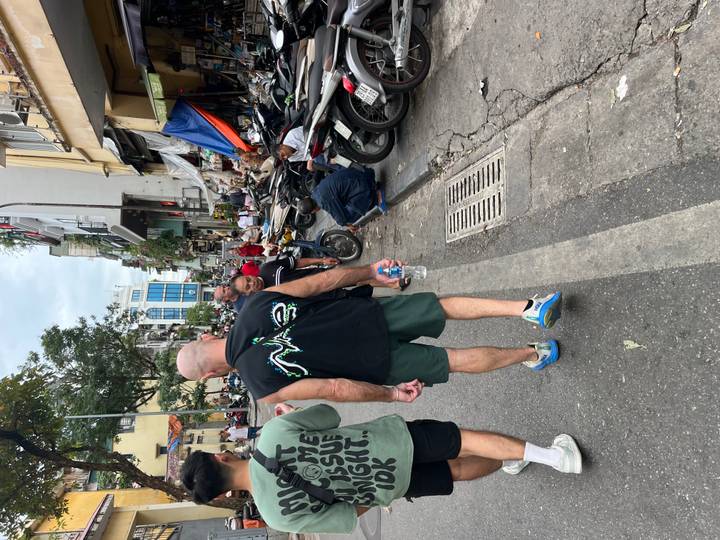 Busy Vietnamese street with motorbikes, vendors and tourists walking past small shops.