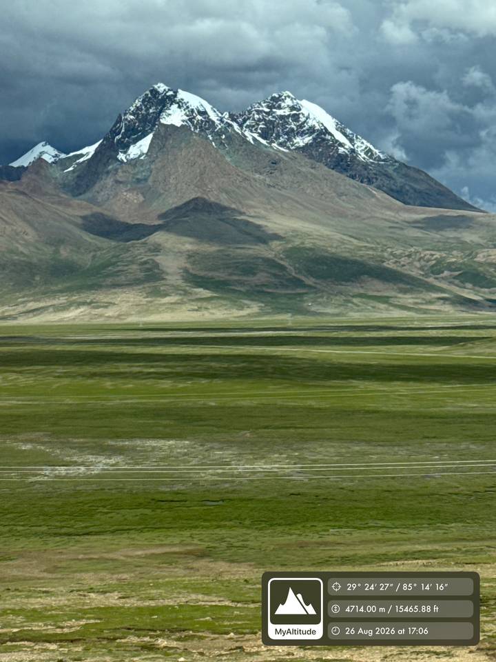 Wide Tibetan plateau of green meadows and distant mountains under soft light.