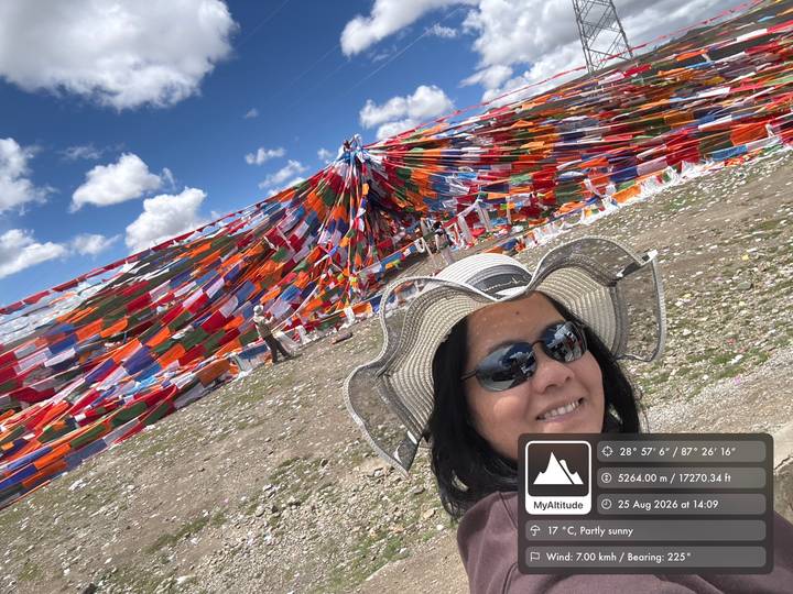 Traveler takes a selfie in front of colorful prayer flags on a sunny Tibetan plateau.