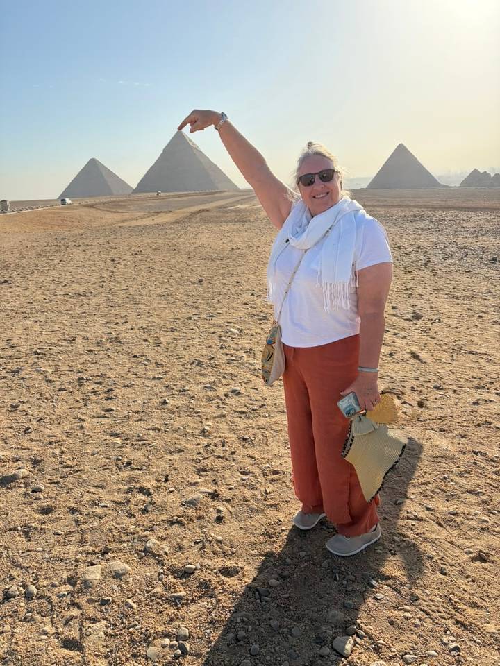 Woman stands in desert landscape playfully posing with woven bag and scarf.