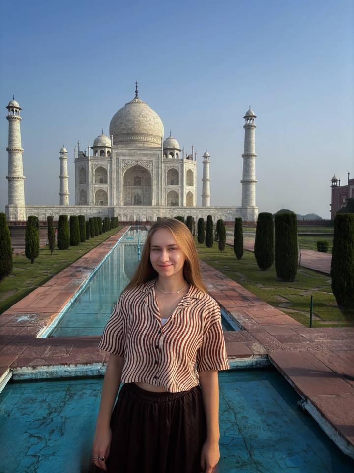 Young woman poses in front of the reflecting pool and pristine white marble Taj Mahal.