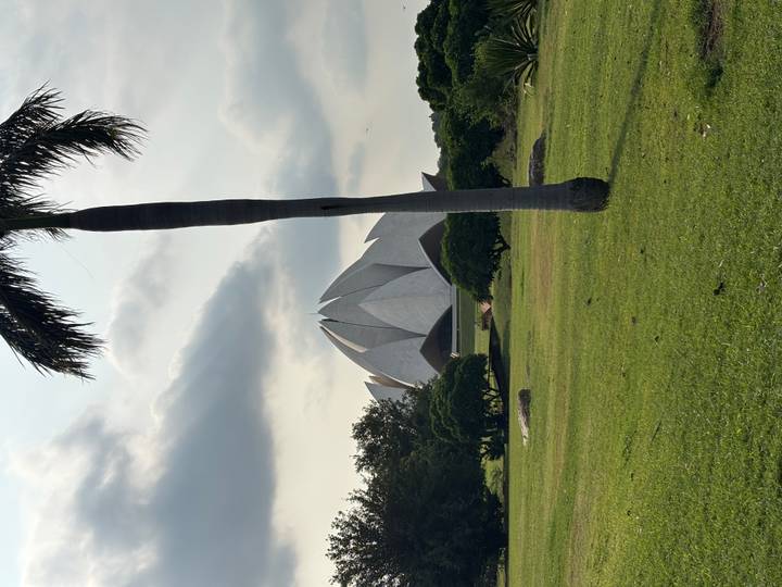 Lotus-shaped white marble temple seen across a green lawn with a palm tree in the foreground