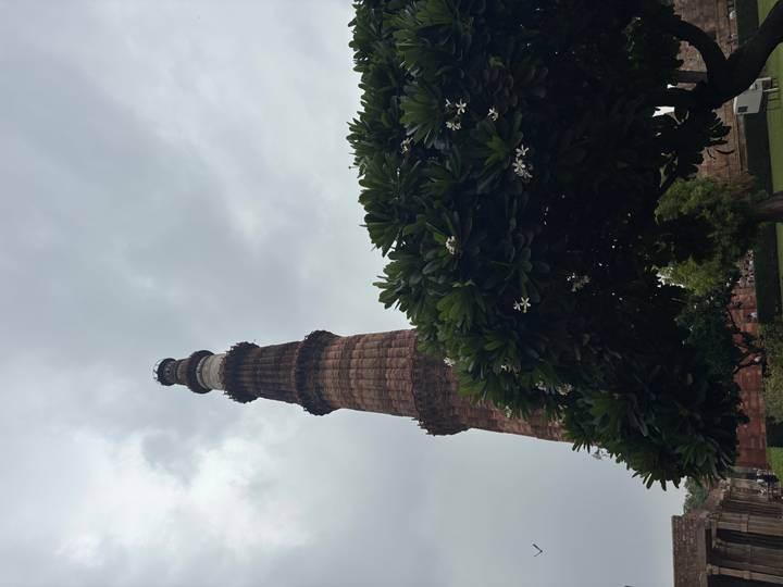 Tall brick minaret rising against a cloudy sky with flowering tree below