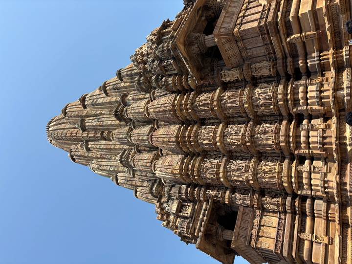 Upward view of an intricately carved sandstone Hindu temple tower against a blue sky
