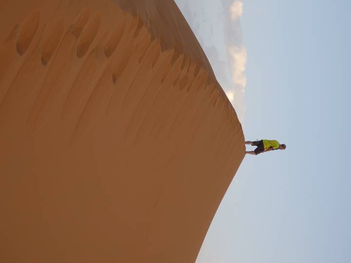 Man standing atop a high orange sand dune at sunset in the Sahara