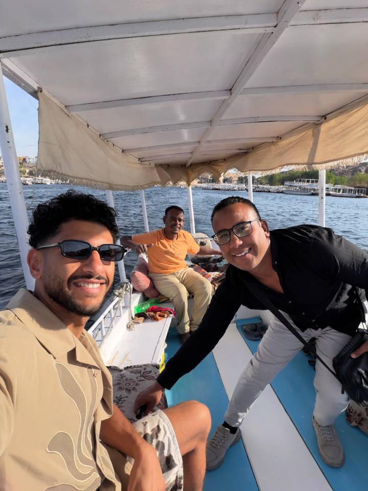 Three men enjoy a small boat ride on a wide river under bright afternoon light.