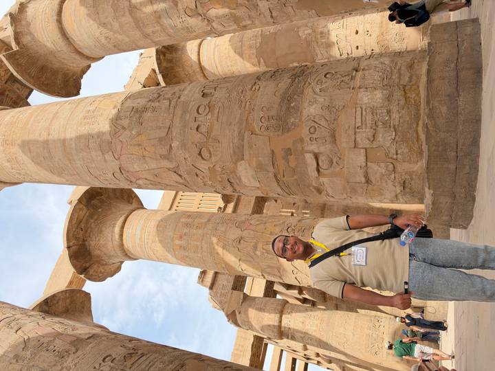 Guide stands before towering hieroglyph-covered columns inside Karnak Temple complex.