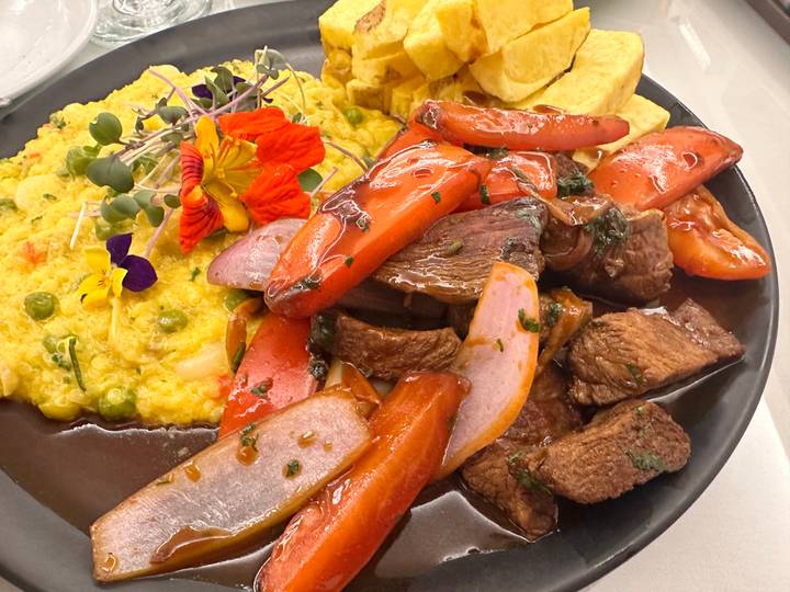 Colorful Peruvian dish with beef, vegetables, and creamy corn accompaniment garnished with flowers.