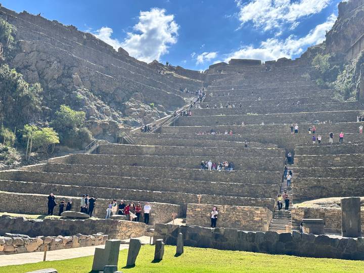 Tourists scale the tiered Inca terraces of Ollantaytambo under bright blue skies.