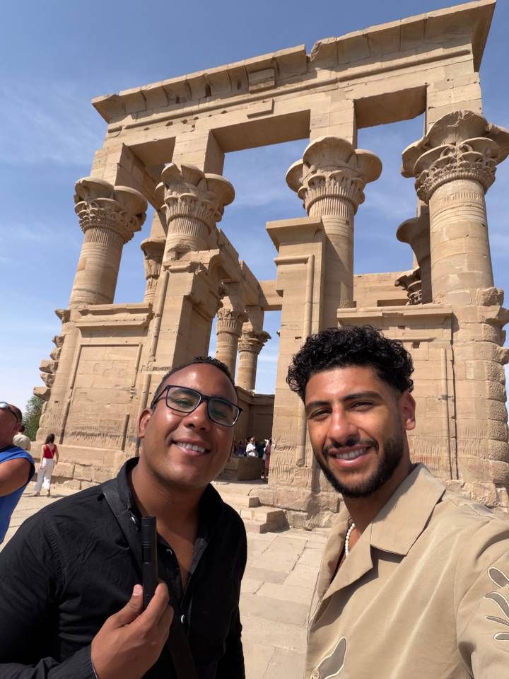 Travelers capture a selfie in front of ornate sandstone columns at Philae Temple in Aswan.