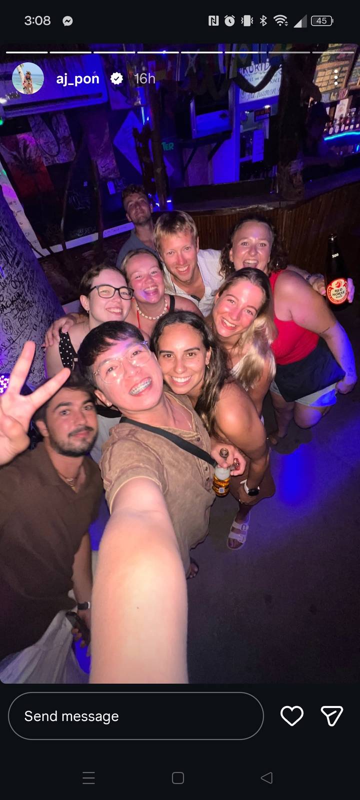 Energetic group selfie at a dimly lit party, travellers smiling and flashing peace signs.