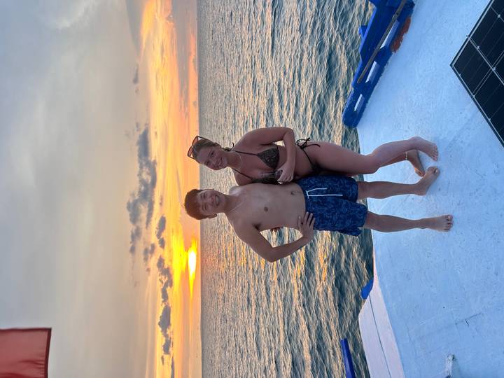 Couple posing on the deck of a boat at sunset with golden reflections over the sea.
