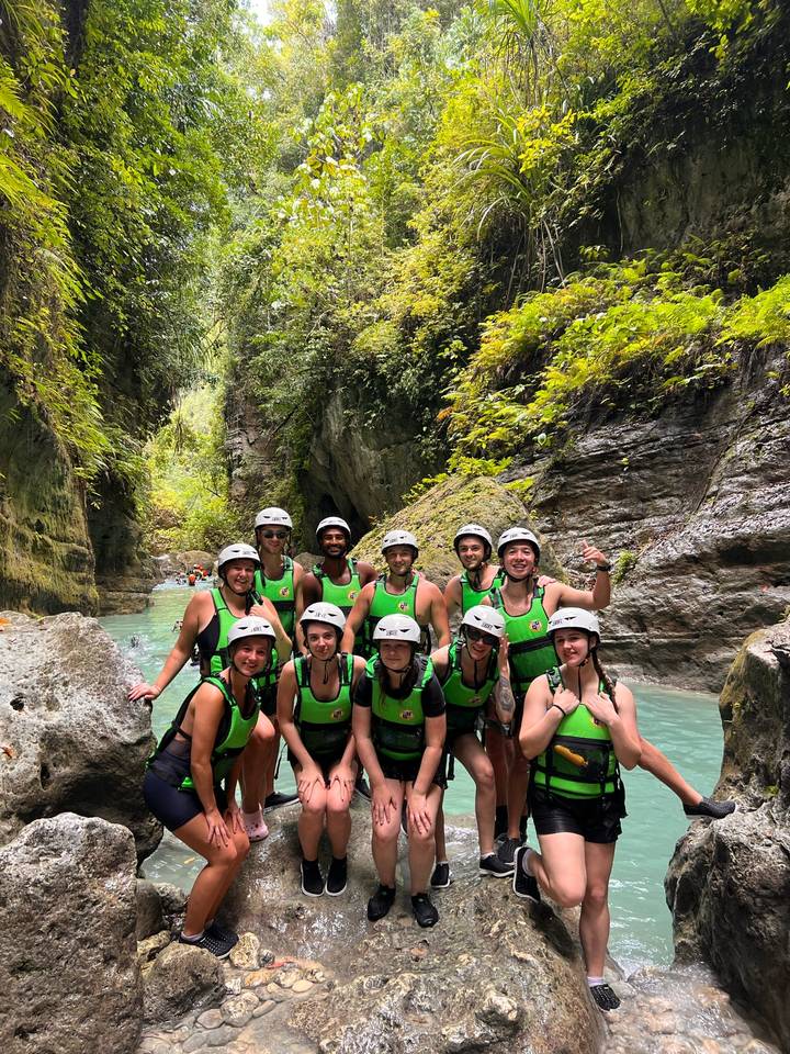 Helmeted adventure group posing in a turquoise canyon river surrounded by lush cliffs.