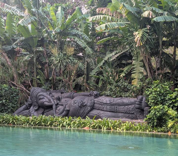 Large reclining stone Hindu deity statue set amid lush tropical foliage in Bali.