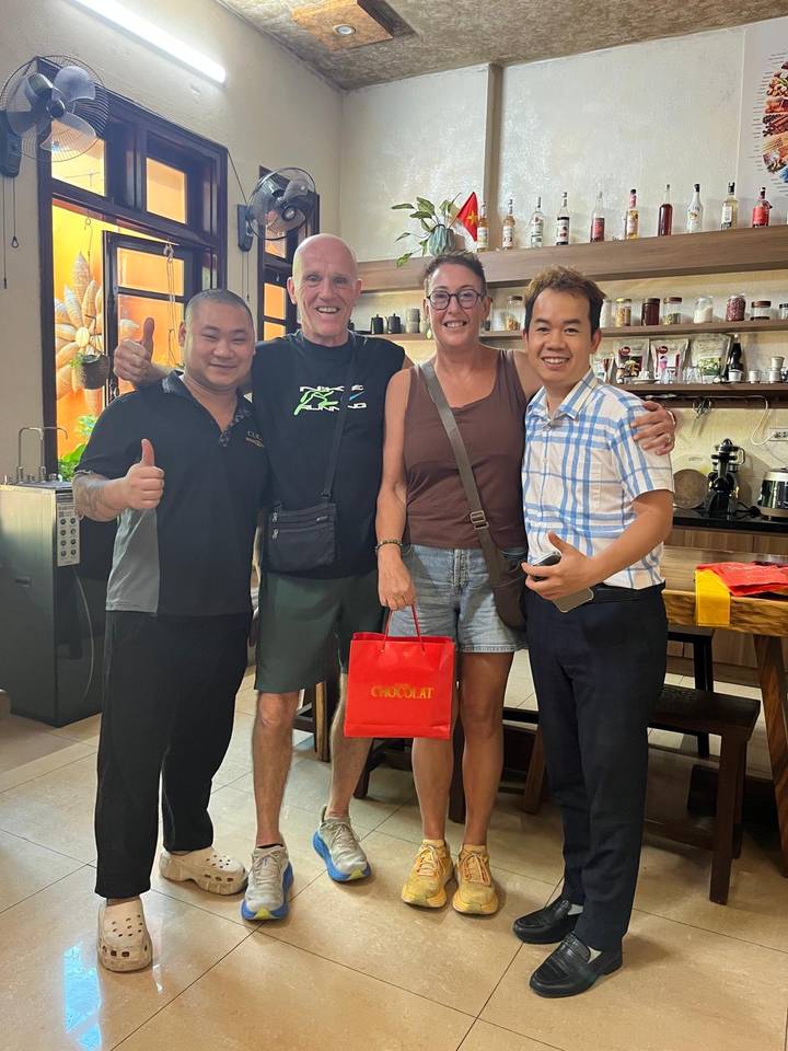 Four people pose inside a café or shop, smiling and holding a red gift bag.